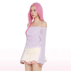 Woman with pink hair wearing a light purple off-shoulder top and cream skirt 