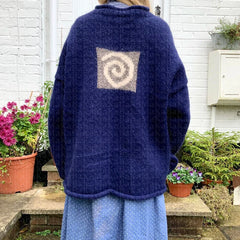 Person wearing a blue sweater with a spiral pattern on the back, standing outdoors.