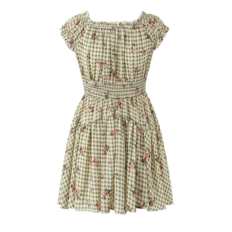 A short, knee-length dress with a green and beige gingham check pattern and scattered small pink and red floral prints. It features an off-the-shoulder neckline, a smocked waist, and ruffled cap sleeves, shown against a plain white background.