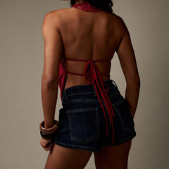 Person wearing a red top and denim shorts with a neutral background