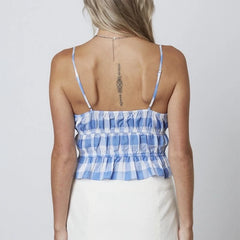 A woman wearing a blue gingham cami top with white jeans, showcasing its versatility and summery style.