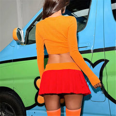 Person wearing an orange top and red skirt standing next to a colorful car.