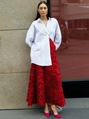 Woman wearing a white shirt and red skirt standing against a building.