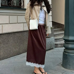 Woman in a beige coat and brown skirt walking on a sidewalk.