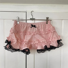 Pink ruffled skirt with black lace trim hanging on a rack against a white paneled wall.