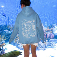 Person wearing a blue jacket with ocean-themed designs in front of an aquarium.