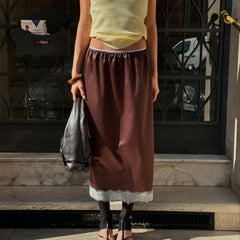 Person wearing a yellow top and brown skirt standing on a street with a building in the background.