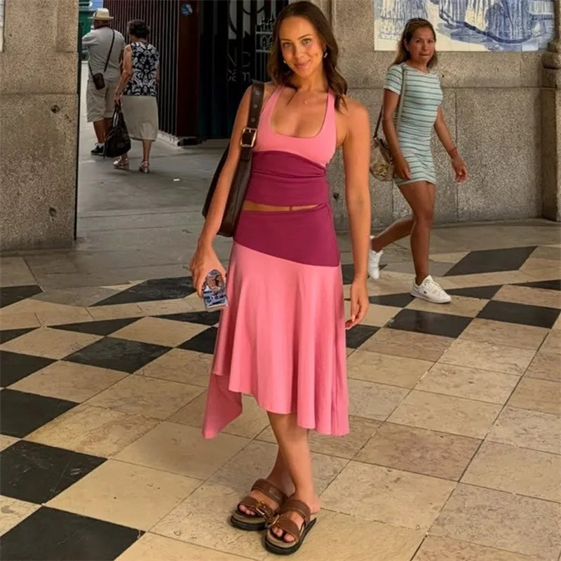 Woman wearing a pink and deep pink two-piece set with a halter crop top and asymmetrical midi skirt, walking on a checkered floor.