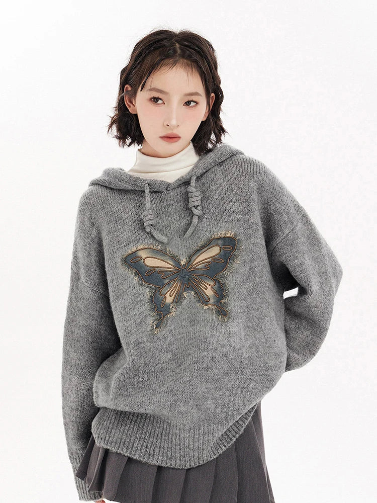 Woman wearing a gray sweater with a butterfly design 
