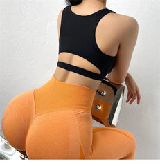 Person wearing a black sports bra and orange leggings on a white background