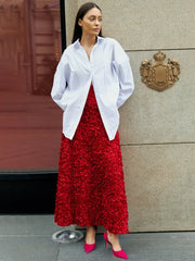 Woman wearing a white blouse and red skirt standing in front of a building entrance.
