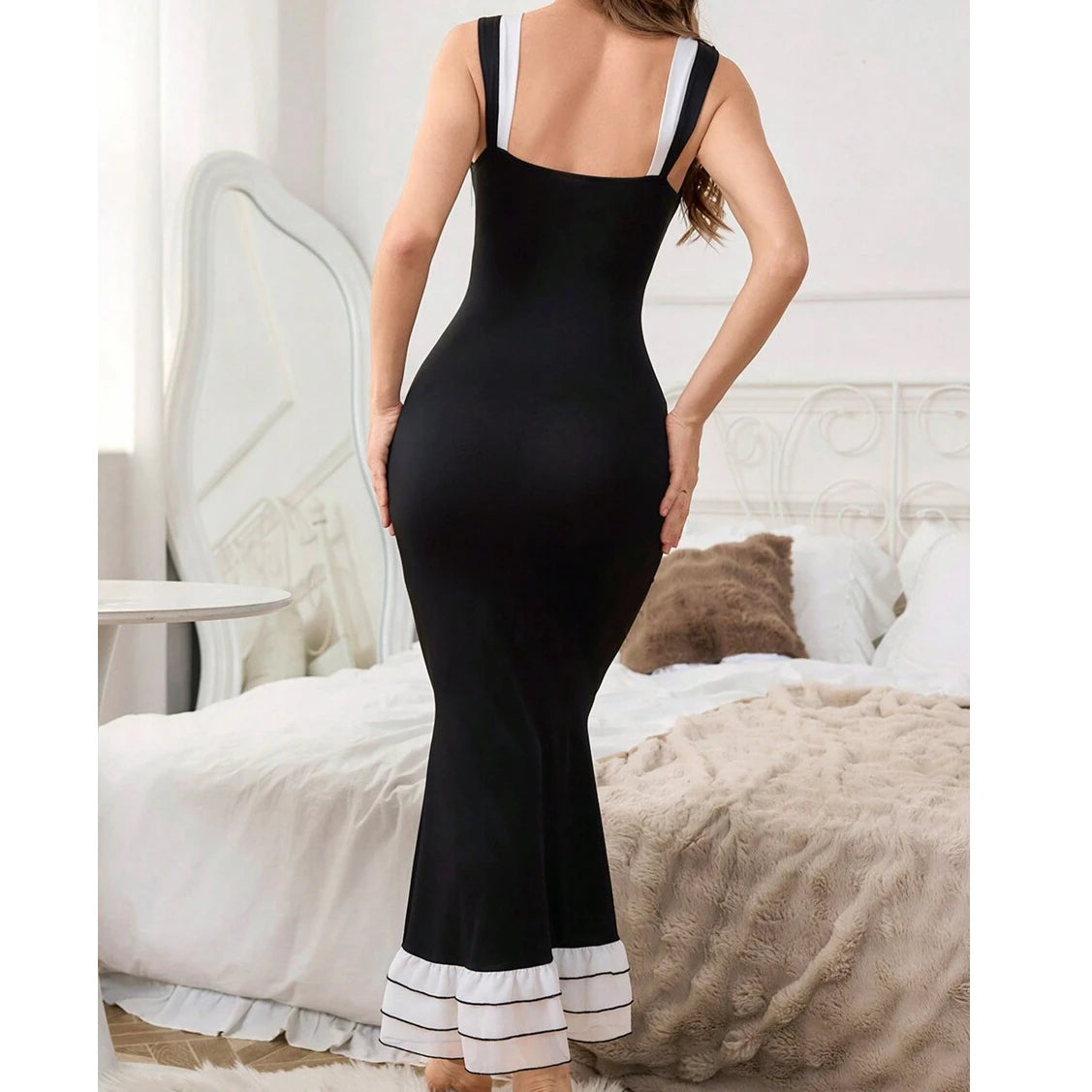 Woman wearing a black dress with white trim in a bedroom setting