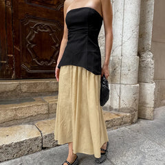 Woman wearing a black strapless top and beige skirt standing in front of a stone building.