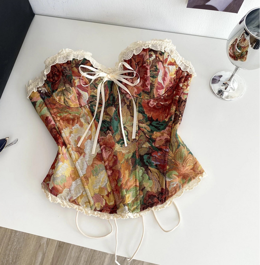 Floral corset on a white surface with sunglasses and a Chanel bag in the background