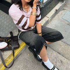 Person sitting on a curb wearing a striped shirt and black pants, with a handbag next to them.