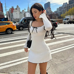 Woman in a white dress standing on a city street with buildings and taxis in the background
