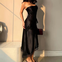 Woman wearing a black one-shoulder dress holding a red handbag indoors.