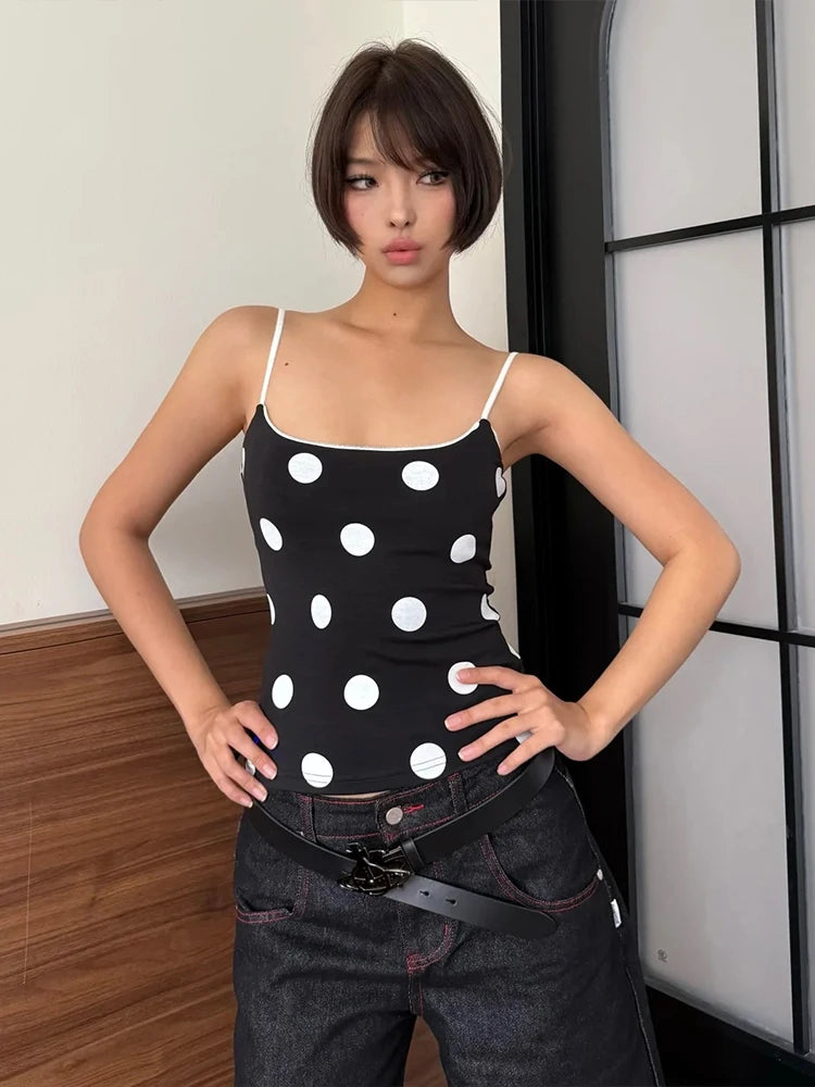 Woman wearing a black tank top with white polka dots and dark jeans indoors.