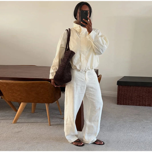 Person taking a mirror selfie wearing a white outfit in a room with wooden furniture.