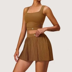 Woman wearing a brown tank top and pleated skirt on a light gray background