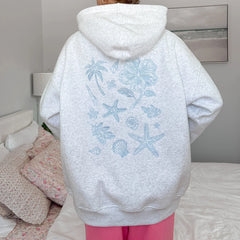 Person wearing a light gray hoodie with blue floral and sea-themed designs, standing in a bedroom.