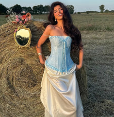 Woman in a blue and white dress standing next to a hay bale with flowers in a field.