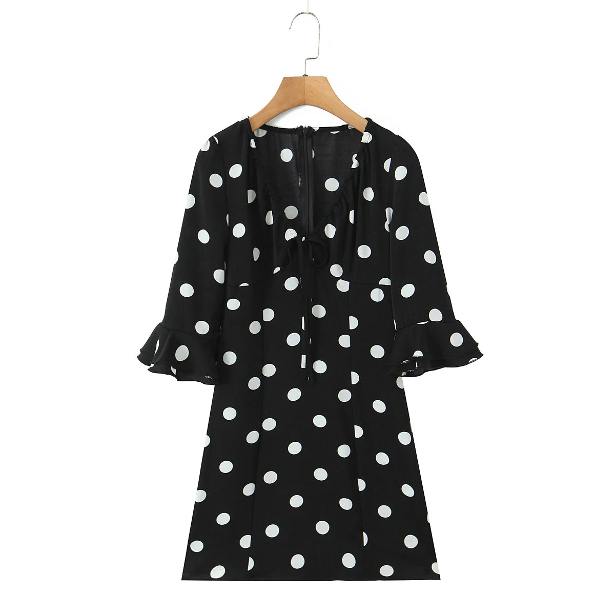 Black dress with white polka dots on a wooden hanger against a white background