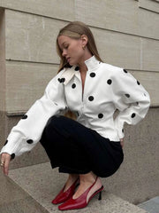 Woman wearing a white blouse with black polka dots and red shoes, sitting on steps.