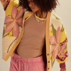 Woman wearing a colorful floral cardigan over a brown top and pink pants on a neutral background