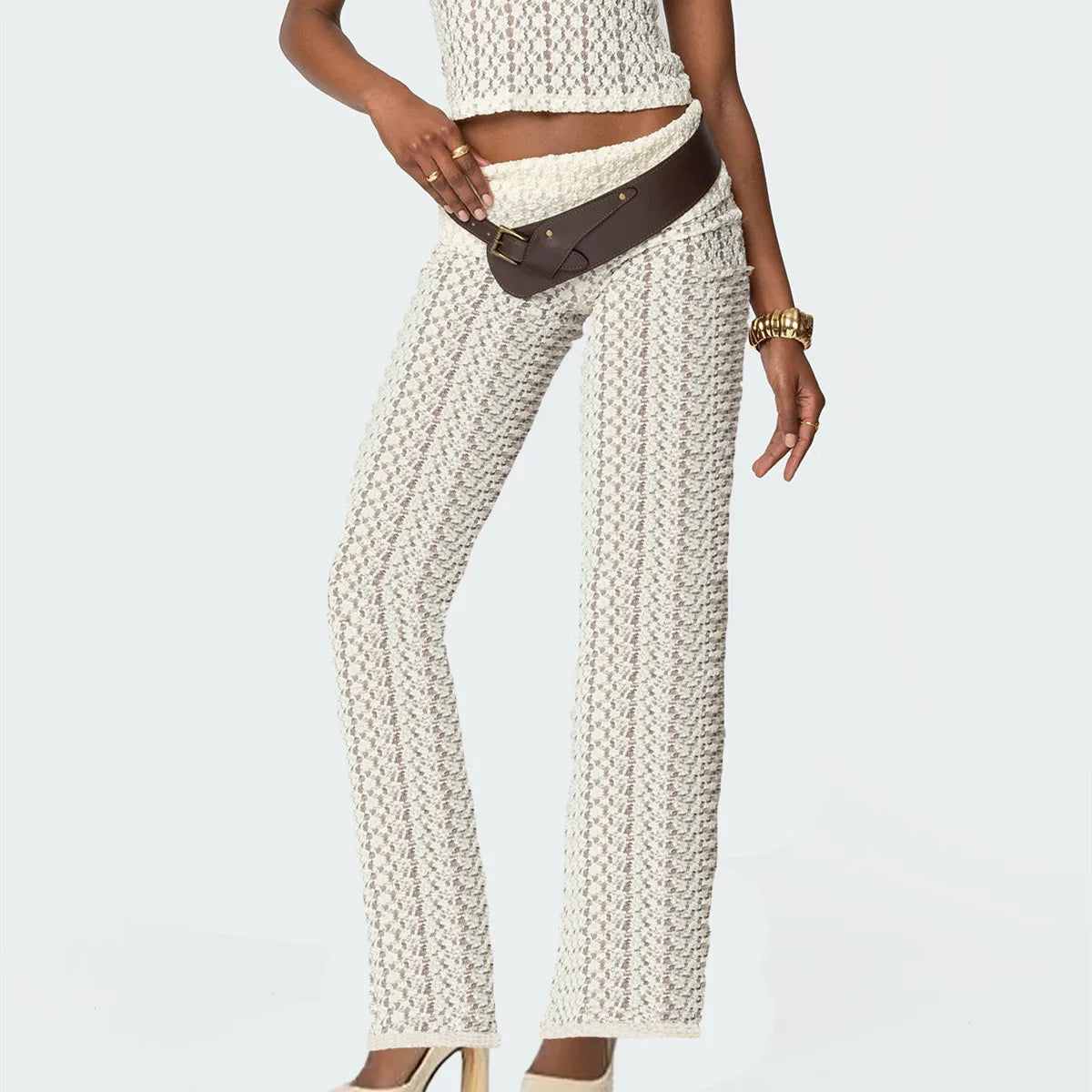 Person wearing a textured white top and pants with a brown belt on a light gray background