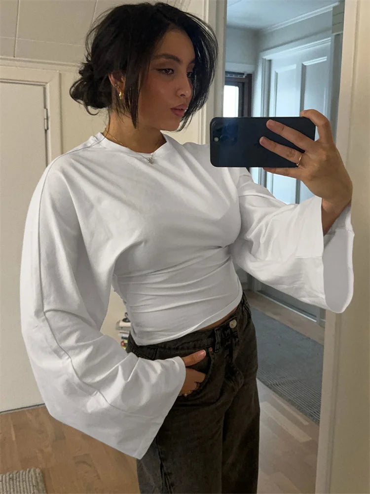 Person taking a mirror selfie wearing a white long-sleeve top and dark pants.
