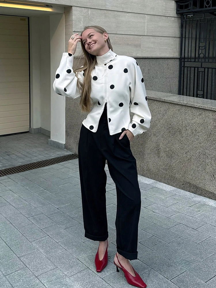 Woman wearing a white polka dot blouse and black pants standing on a sidewalk.