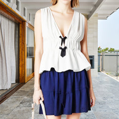 Woman wearing a white top with black details and a blue skirt in an outdoor setting.