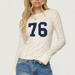 Woman wearing a white long-sleeve shirt with blue number '76' and floral pattern, paired with blue jeans