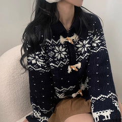 Person wearing a navy blue knitted cardigan with white patterns sitting on a beige chair.