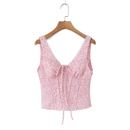 A pink floral sleeveless crop top with a lace-trimmed V-neckline, front tie detail, and lace-up side corset-style closures, hanging on a wooden hanger against a plain white background.