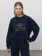 Woman wearing a navy blue sweatshirt with 'La Vie En Rose' text on a plain background