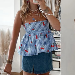 A woman wearing a blue cherry plaid cami top with white jeans, showcasing its versatility and flattering fit.