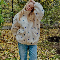 Person wearing a cream-colored sweater with blue floral patterns in an autumn setting.