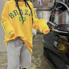 Person wearing a yellow 'BRAZIL' sweatshirt with a car in the background