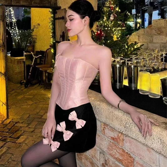 Woman in a black dress with pink bows standing in a festive indoor setting.