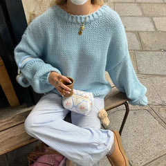 Person wearing a light blue sweater and white pants, sitting on a bench holding a cup.
