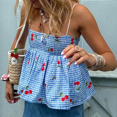 A woman wearing a blue cherry plaid cami top with white jeans, showcasing its versatility and flattering fit.