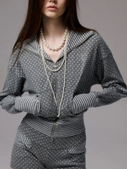Person wearing a gray polka dot outfit with striped cuffs and a pearl necklace 