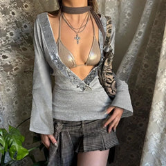 Person wearing a gray cardigan over a metallic top and plaid shorts against a patterned curtain background.