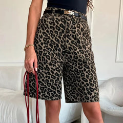 Person wearing leopard print shorts holding a red bag indoors.