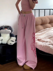 Person wearing pink sweatpants with a logo in a bedroom setting