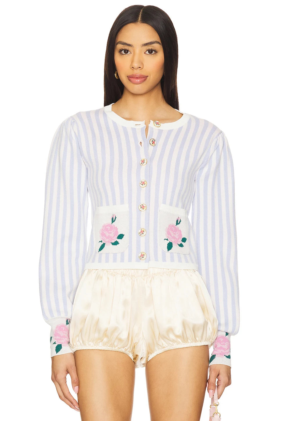 A model wearing a light blue and white vertically striped long-sleeve cardigan with pink rose embroidery on the pockets and cuffs, paired with cream satin bubble shorts, against a plain white background.