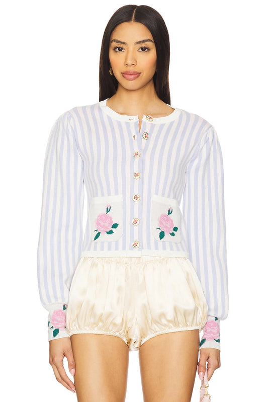 A model wearing a light blue and white vertically striped long-sleeve cardigan with pink rose embroidery on the pockets and cuffs, paired with cream satin bubble shorts, against a plain white background.