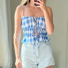 A woman wearing a blue gingham cami top with white jeans, showcasing its versatility and summery style.